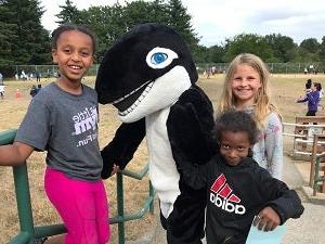 Three students stand together with a school mascot 虎鲸